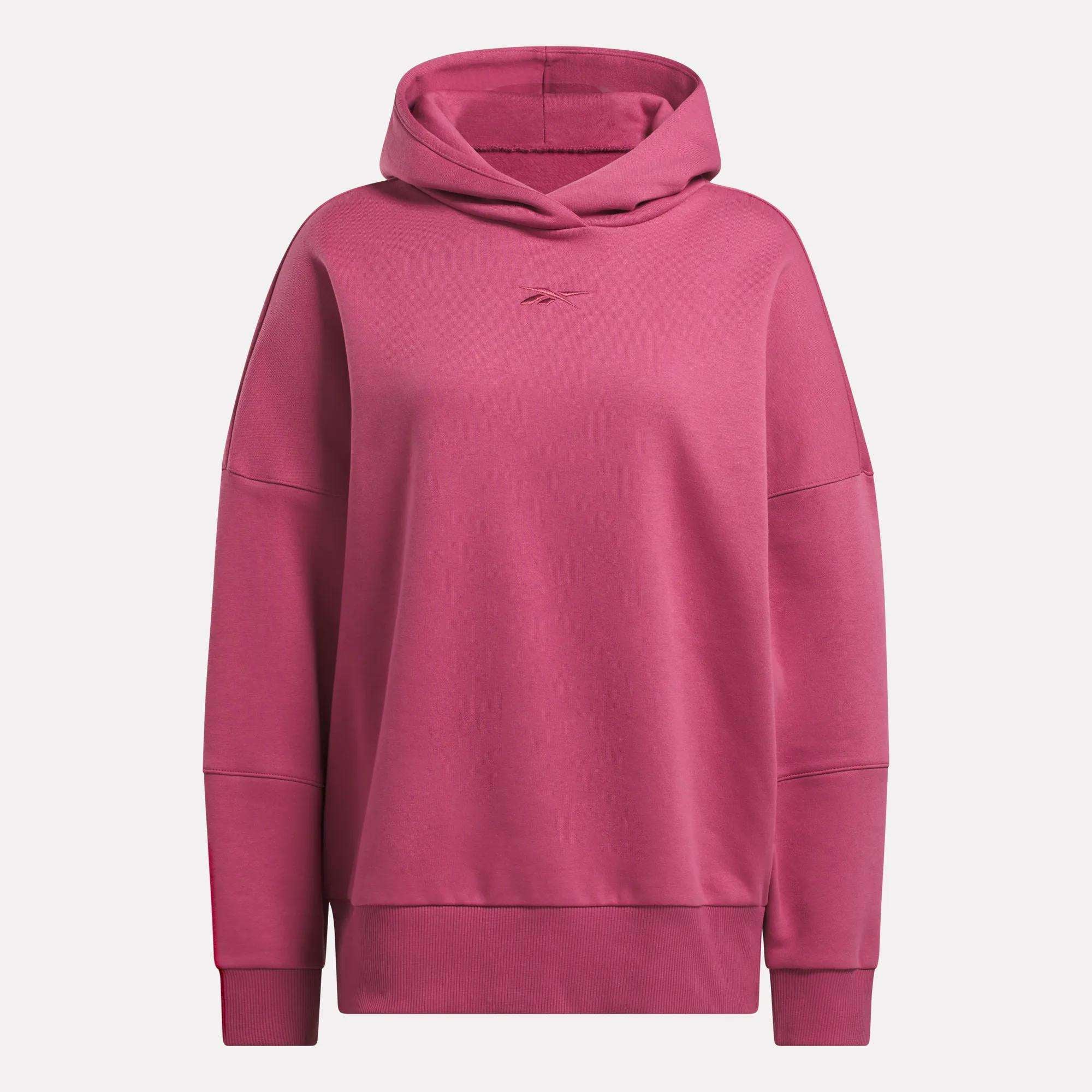The Reebok Women's Lux Hoodie is a cozy, long-sleeved hoodie in solid rose pink with minimal seams and a small chest logo—perfect as an oversized option for laid-back comfort.