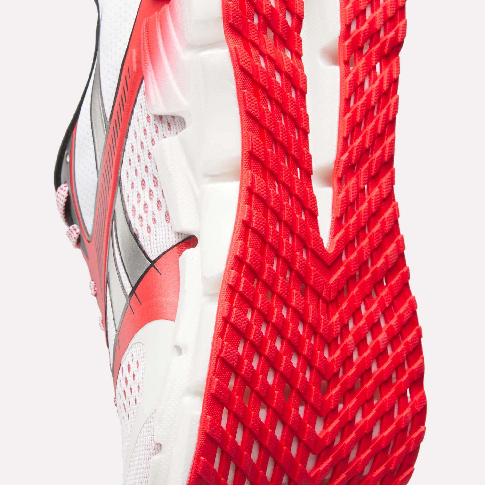 Close-up of the sole and side of the Reebok Men's FloatZig 2 AHA Running Shoes, featuring red and black accents, a textured red tread pattern, mesh upper, and energy-returning cushioning for enhanced comfort.
