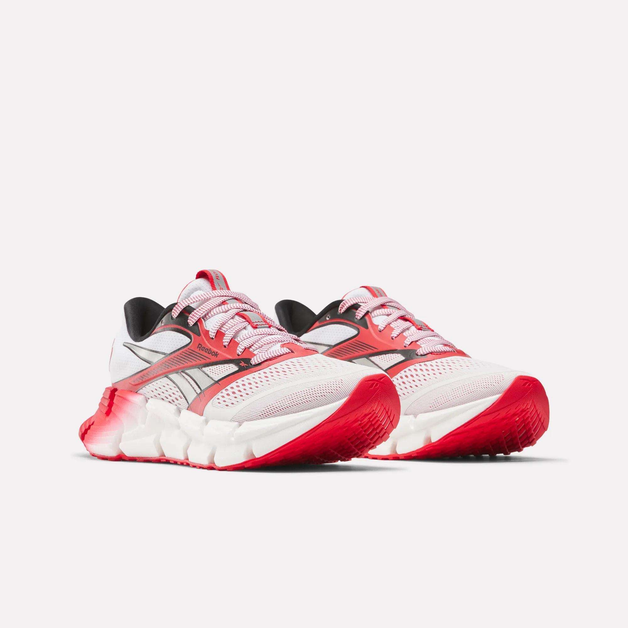 The Men's FloatZig 2 AHA Running Shoes by Reebok feature white mesh uppers, red accents, black details, chunky midsoles, bright red textured soles for comfort, energy-returning cushioning, and stylish white and pink laces.