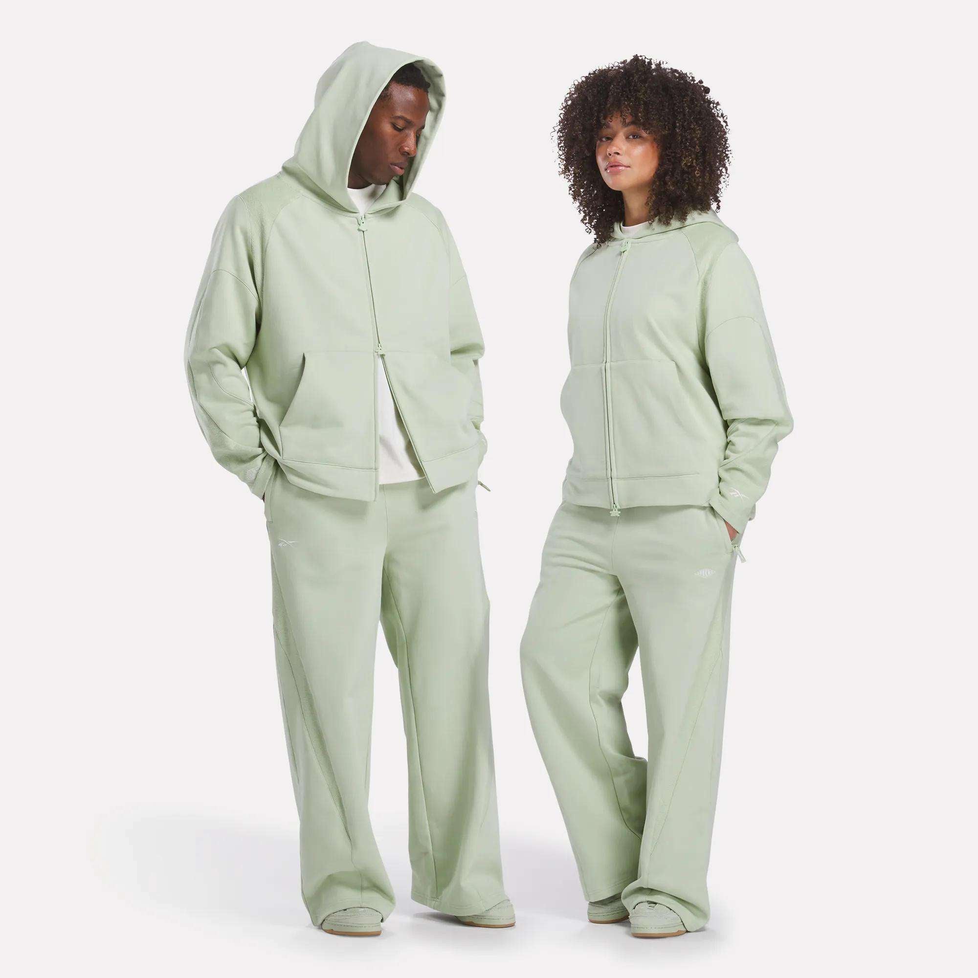 A man and woman wear matching Reebok x CHUKWU Full-Zip Hoodies, crafted from soft French terry.