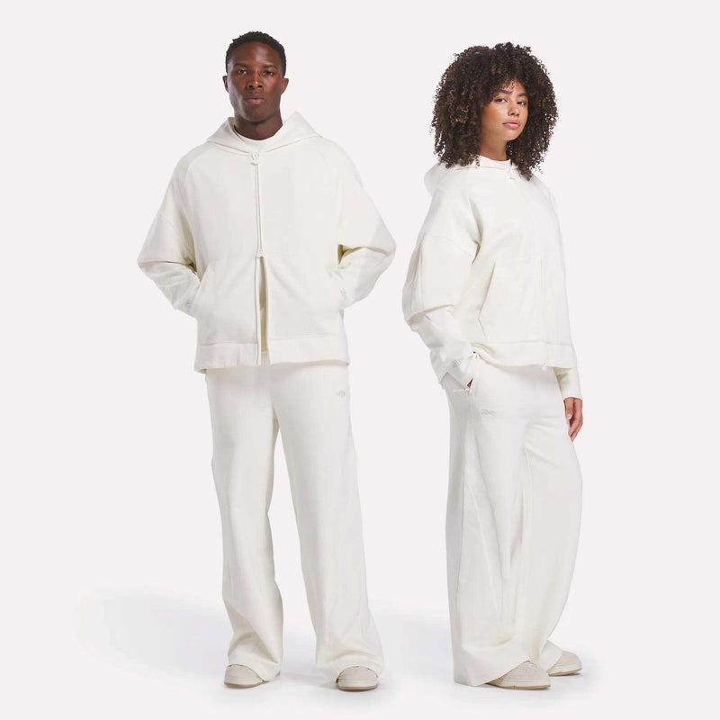 Two people wear matching Reebok x CHUKWU Full-Zip Hoodies, hands in their pockets, as they pose effortlessly against a plain white background.