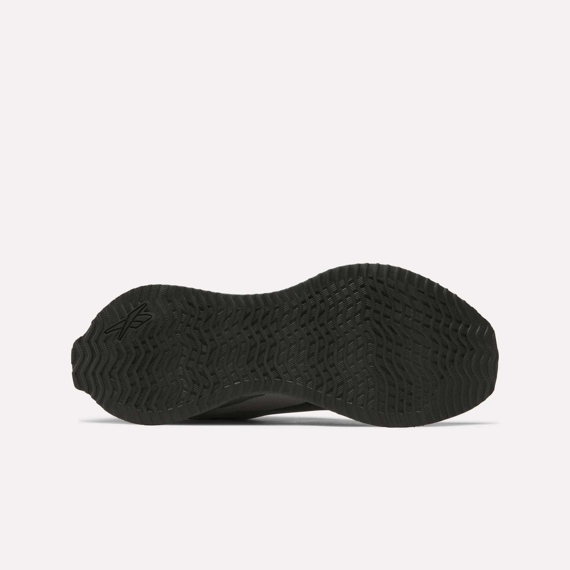 The image shows the black, textured rubber outsole of the Reebok Zig Dynamica STR Shoes, viewed from the bottom. It features a wave-like tread pattern, a small logo on the left side, and a plain, light-colored background.