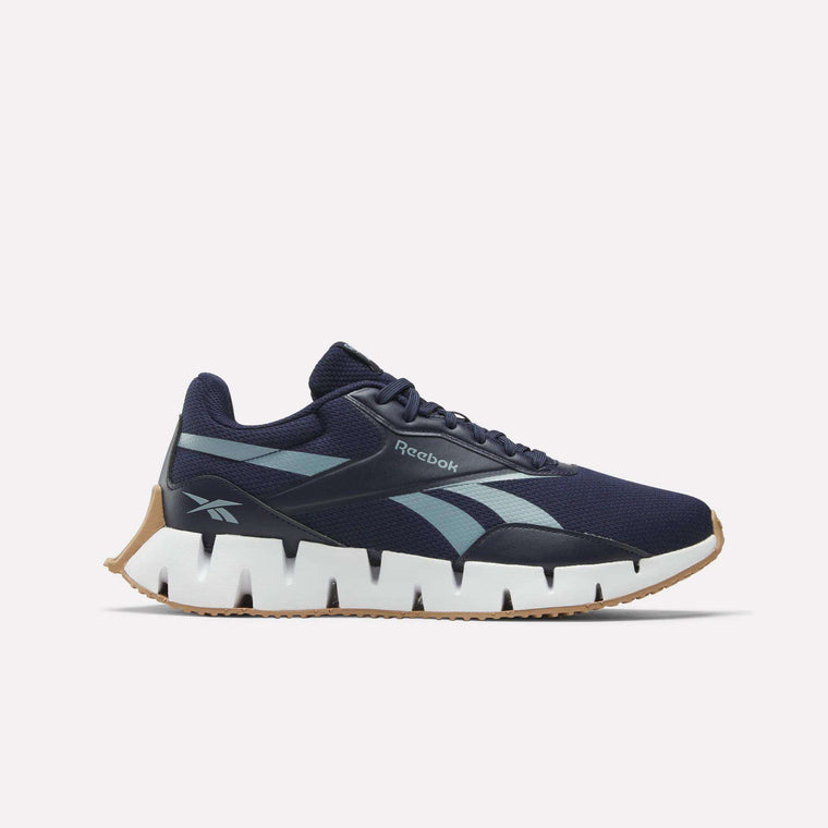 The Reebok Zig Dynamica STR Shoes in navy blue feature a white and gum sole, light blue Reebok logos, a zigzag midsole pattern, and a breathable mesh upper. This innovative athletic shoe is shown from the side on a plain white background.