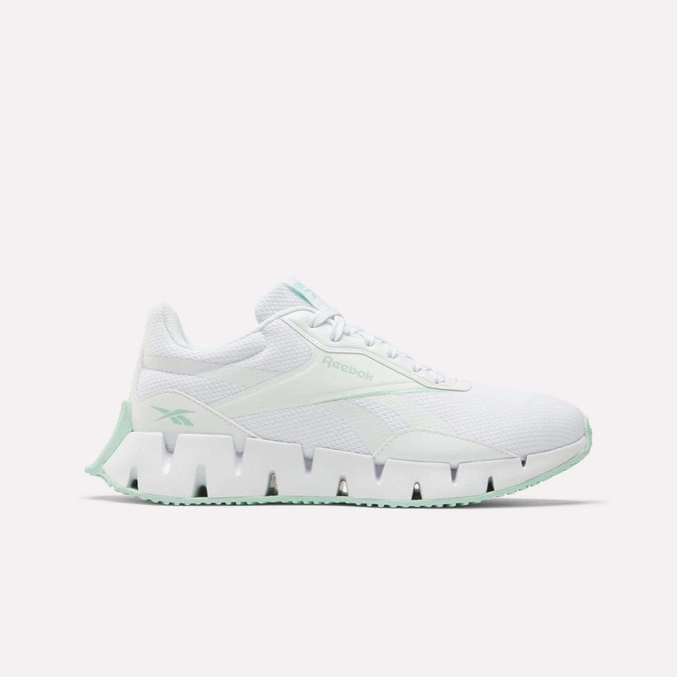 The Women's Zig Dynamica STR Shoes by Reebok feature a white design with a chunky, futuristic sole, light green accents, and breathable mesh details for comfort, shown against a plain white background.
