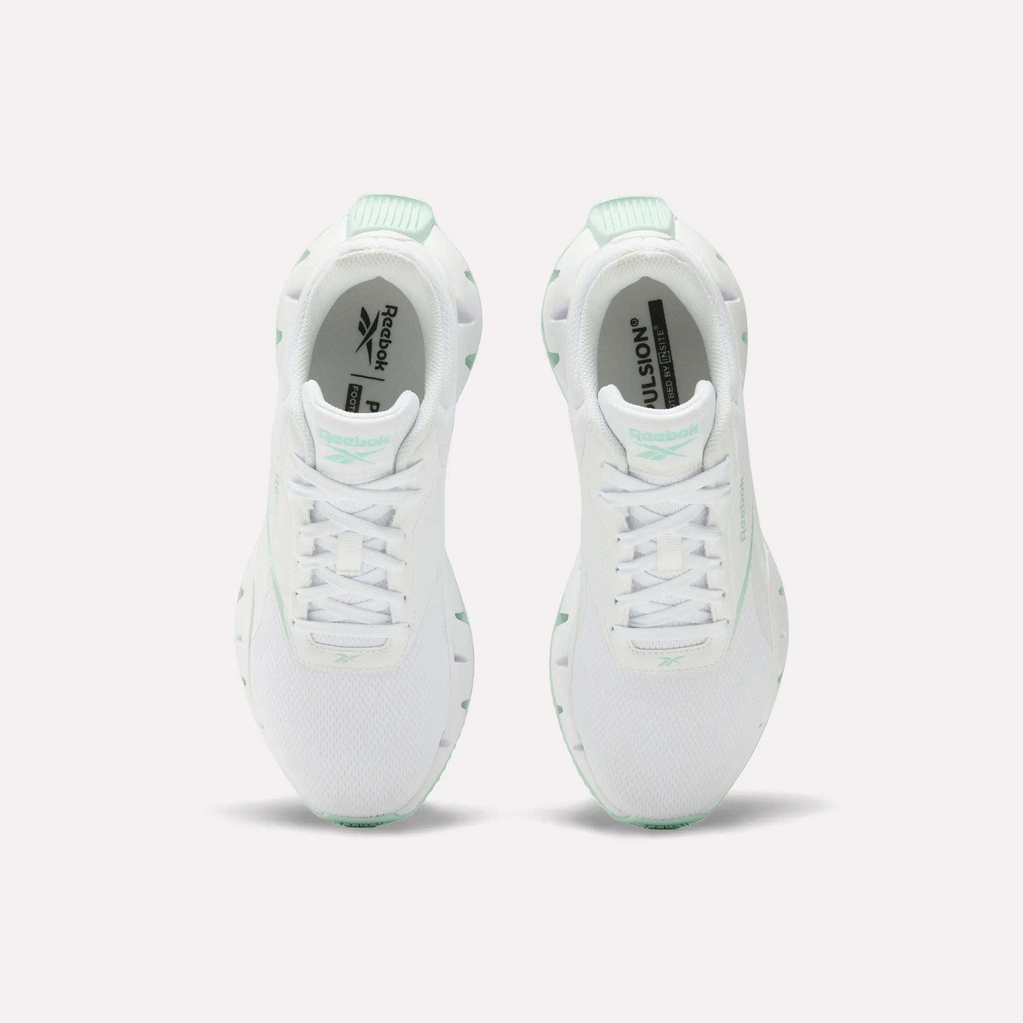 A pair of Reebok Women's Zig Dynamica STR Shoes in white with mint green accents, featuring breathable mesh for comfort, shown from above on a plain white background.