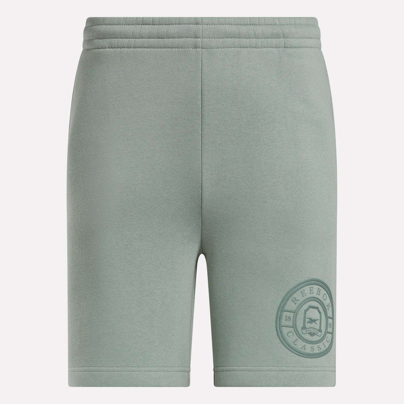 Light green Men's Crest Shorts by Reebok featuring a relaxed fit, elastic waistband, soft cotton fabric, and a darker green circular Reebok Classic logo near the left hem. Front view shown.