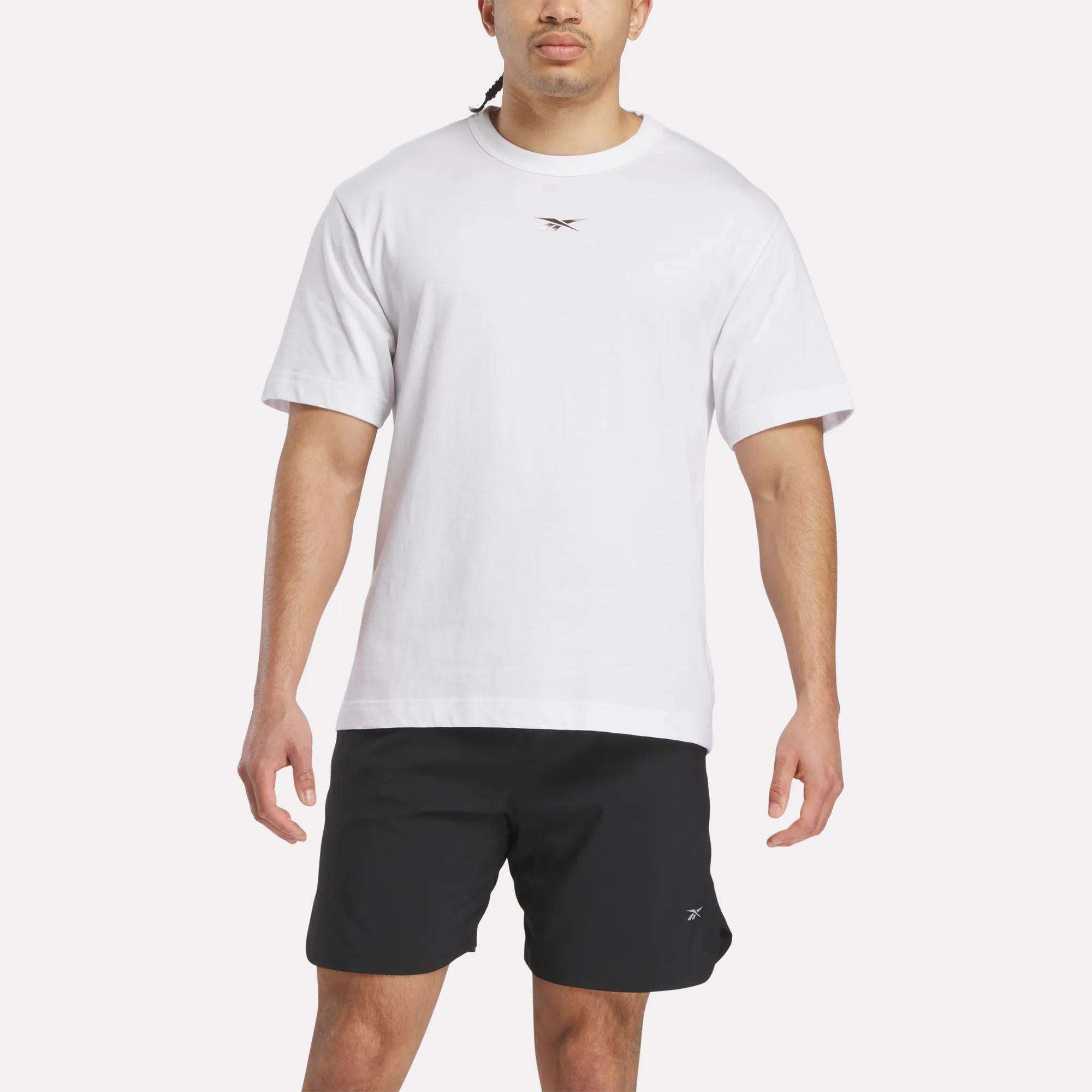 A man faces forward wearing a Reebok Men's Athlete Speed Logo T-Shirt in soft cotton-blend jersey with a small chest logo and black shorts with a left-leg logo, set against a plain light background.