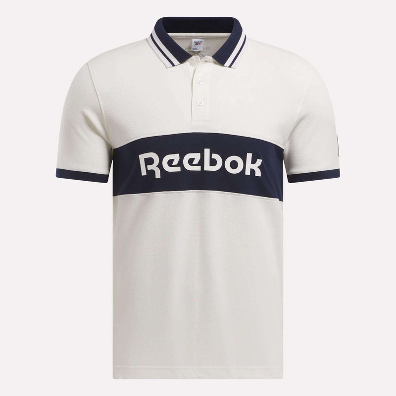The Men’s Lawn Club Polo Shirt by Reebok is crafted in a soft cotton blend, featuring navy stripes on the collar and sleeves and a bold navy chest band with a white Reebok logo.