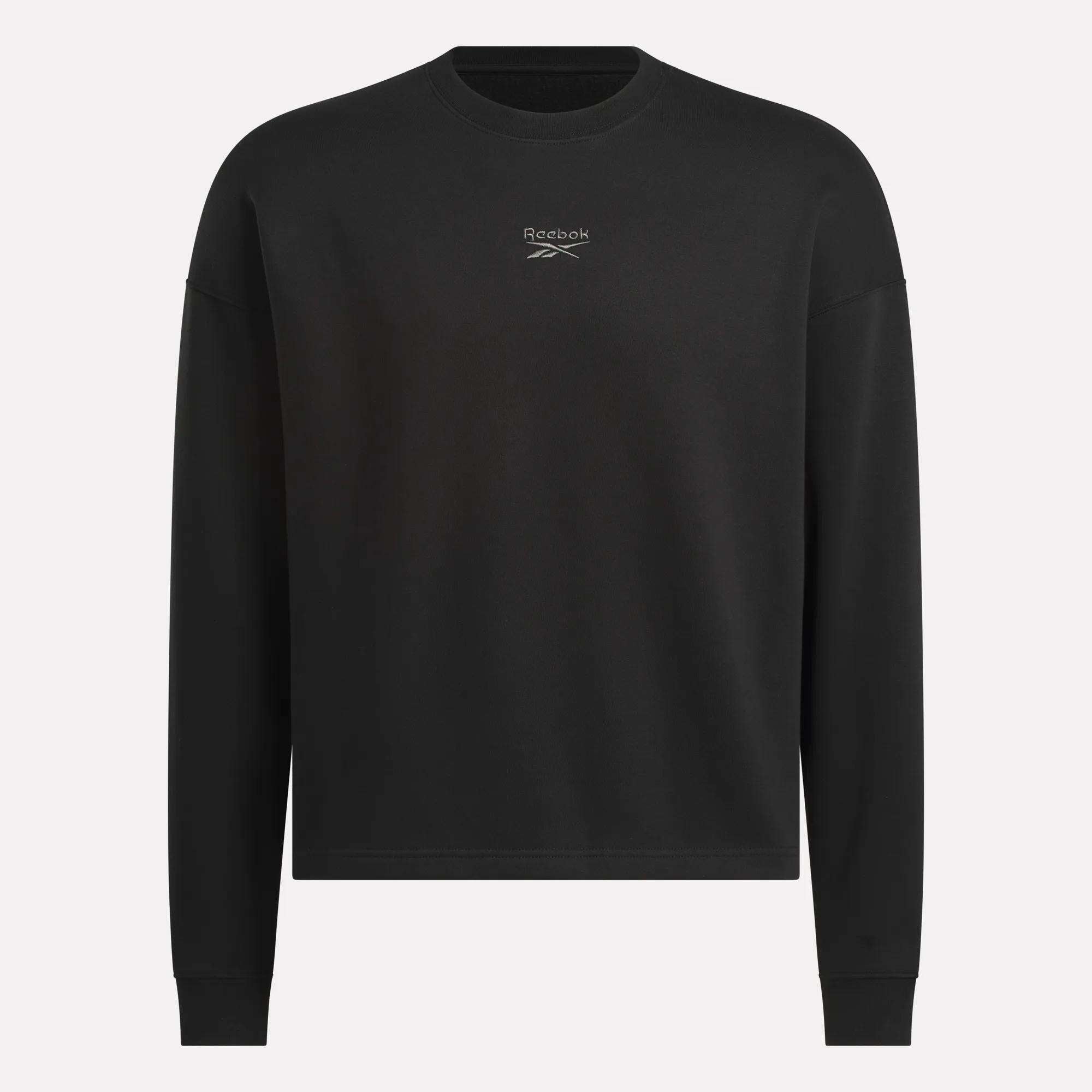 The Men's Wardrobe Essentials Sweatshirt by Reebok is a plain black, relaxed-fit design with long sleeves and a small white logo on the chest. Made from soft cotton-blend fleece. Shown against a light gray background.