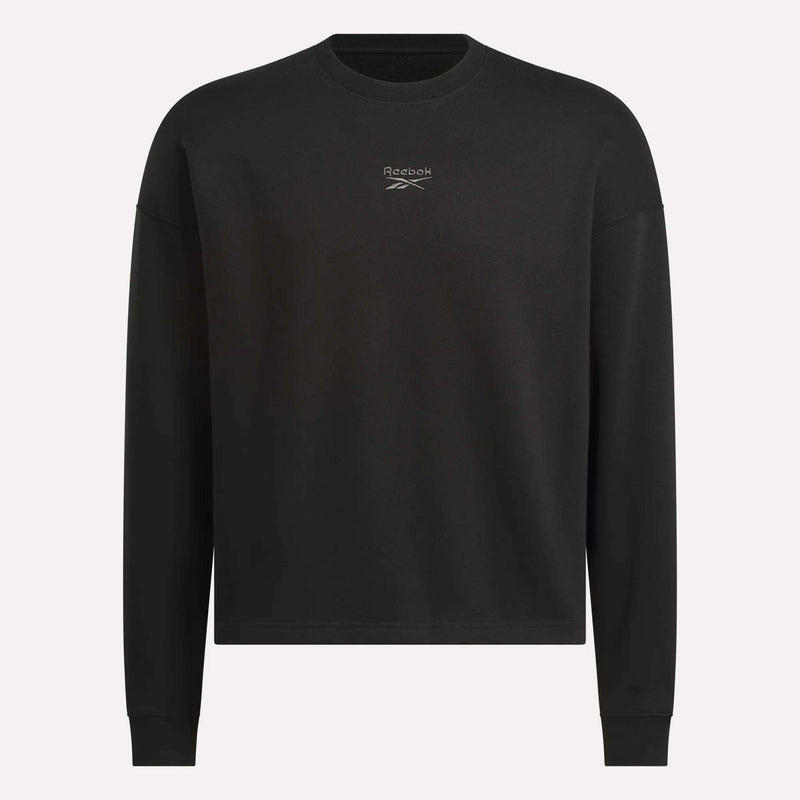 The Men's Wardrobe Essentials Sweatshirt by Reebok is a plain black, relaxed-fit design with long sleeves and a small white logo on the chest. Made from soft cotton-blend fleece. Shown against a light gray background.
