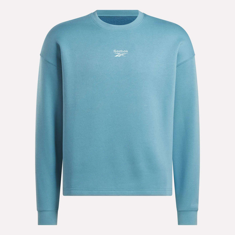 The Men's Wardrobe Essentials Sweatshirt by Reebok is light blue with a relaxed fit, long sleeves, and a small white logo and text on the chest, crafted from soft cotton-blend fleece and shown on a plain white background.