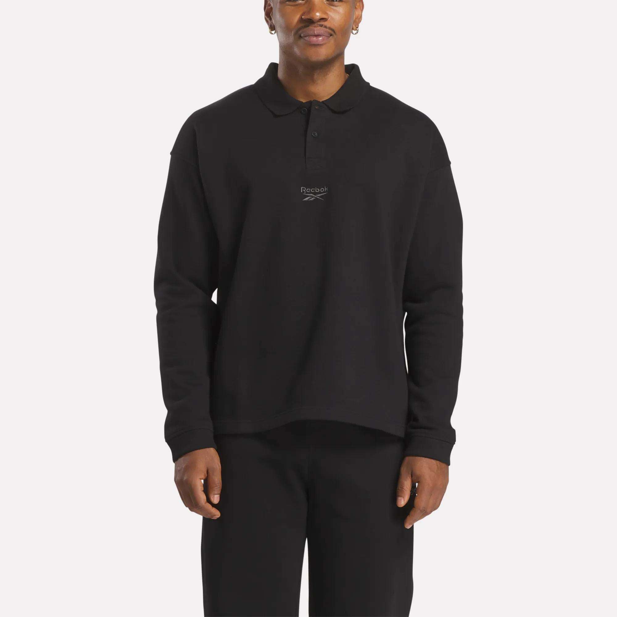 A man wears the Reebok Men's Wardrobe Essentials Long Sleeve Polo Shirt with a chest logo and relaxed fit, standing against a plain white background.