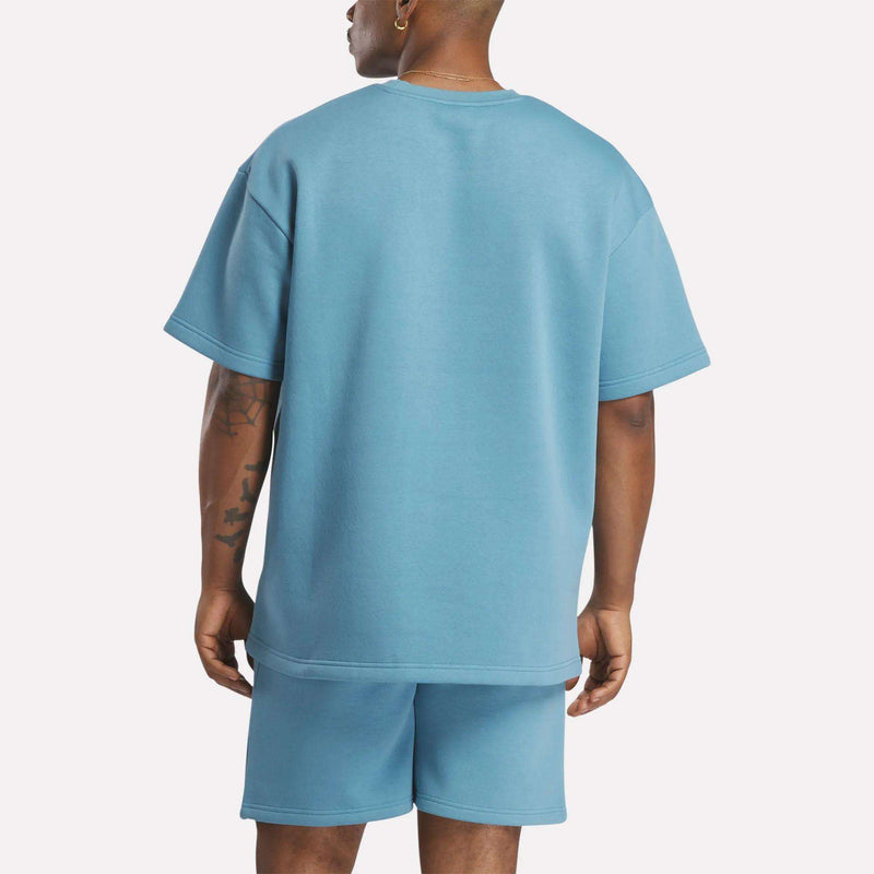 A person is seen from the back wearing a light blue Men's Wardrobe Essentials T-Shirt by Reebok and matching shorts, standing against a plain white background.