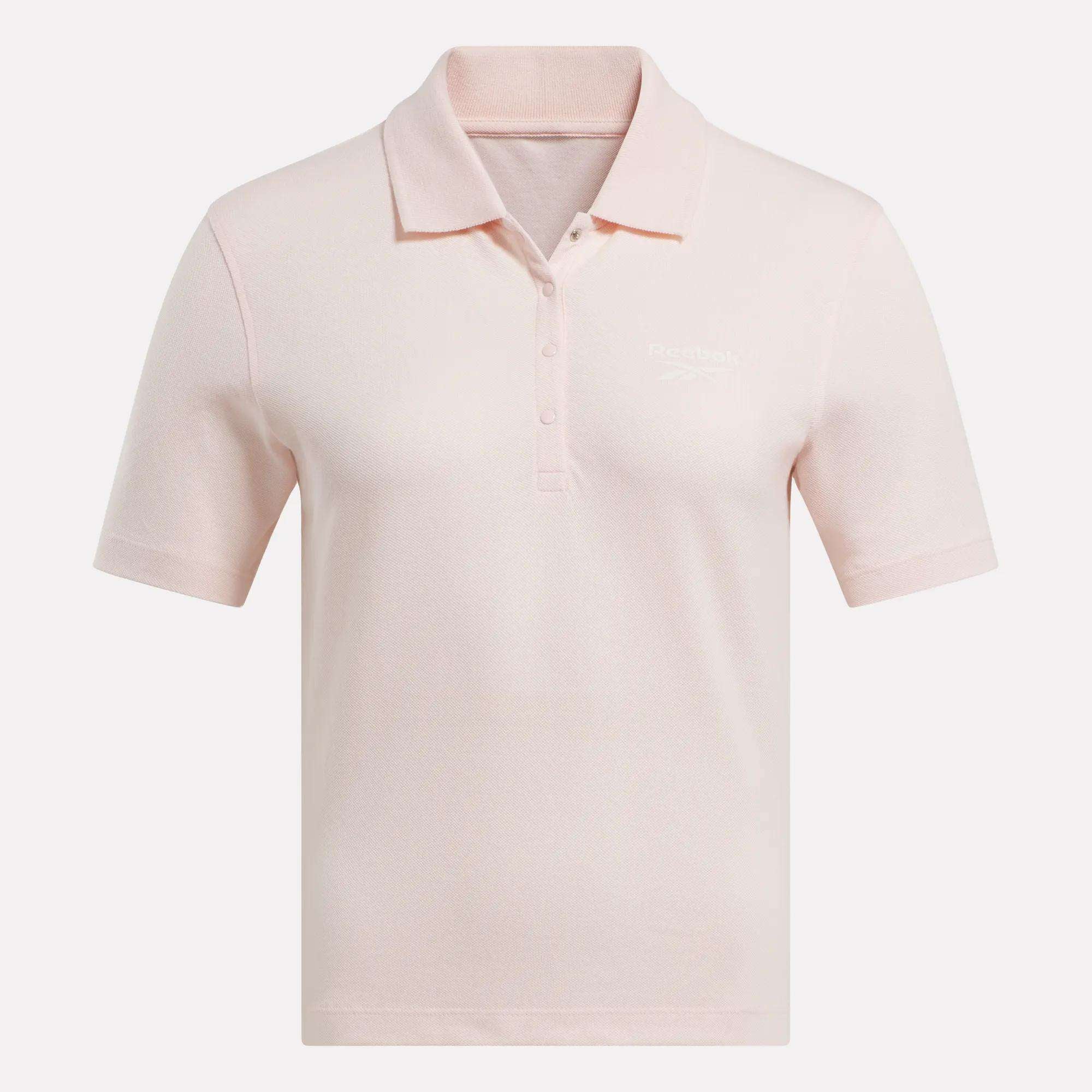 The Women's Fitted Polo Shirt by Reebok is a light pink, stretchy cotton top with short sleeves, a three-button collar, and a subtle embroidered logo on the left chest, shown on a plain white background.
