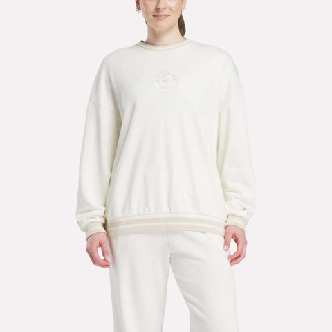 A person wears an oversized, white Women's Lawn Club Crew Sweatshirt by Reebok with subtle chest embroidery and matching white pants, standing against a plain light background.