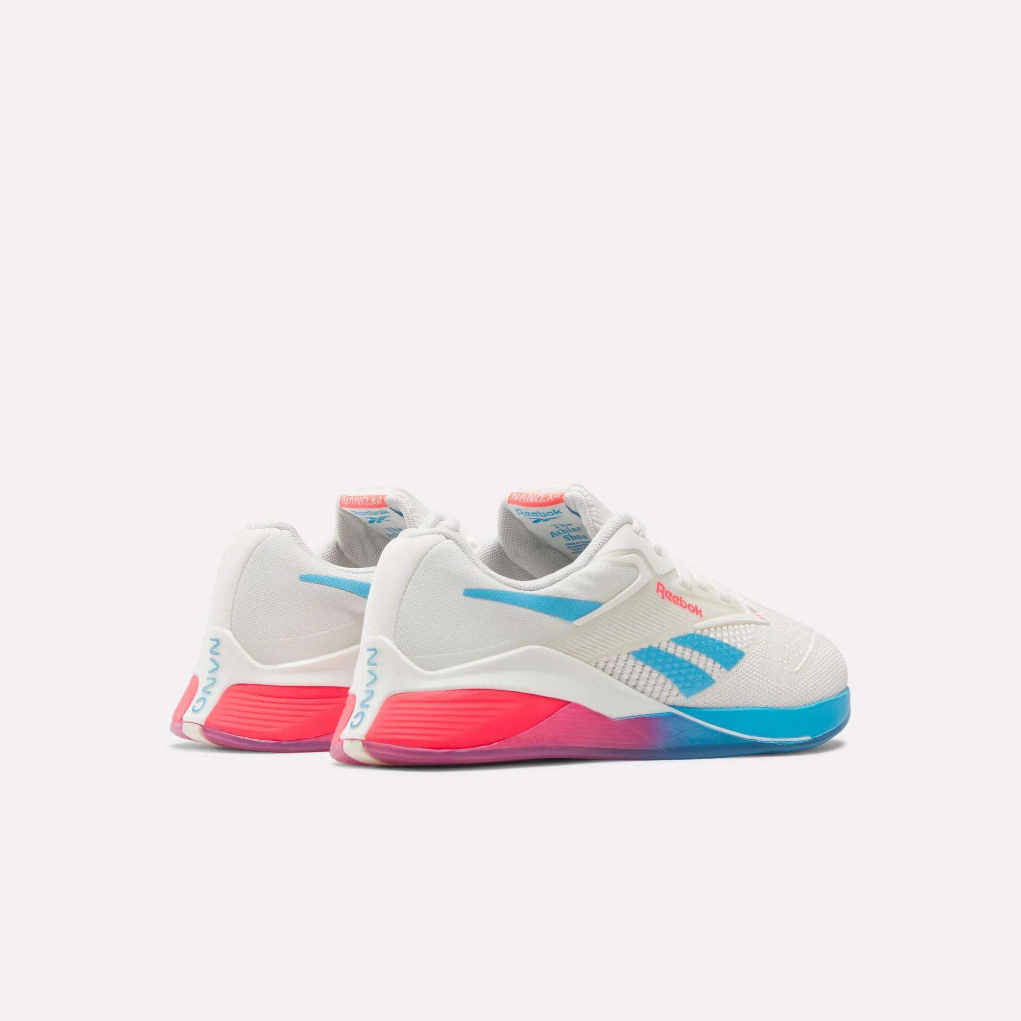 The Women's Nano X4 Training Shoes by Reebok are white with blue and pink accents, featuring a blue logo, stripe details, and pink branding on the heel and tongue. These lightweight shoes are shown on a plain white background.
