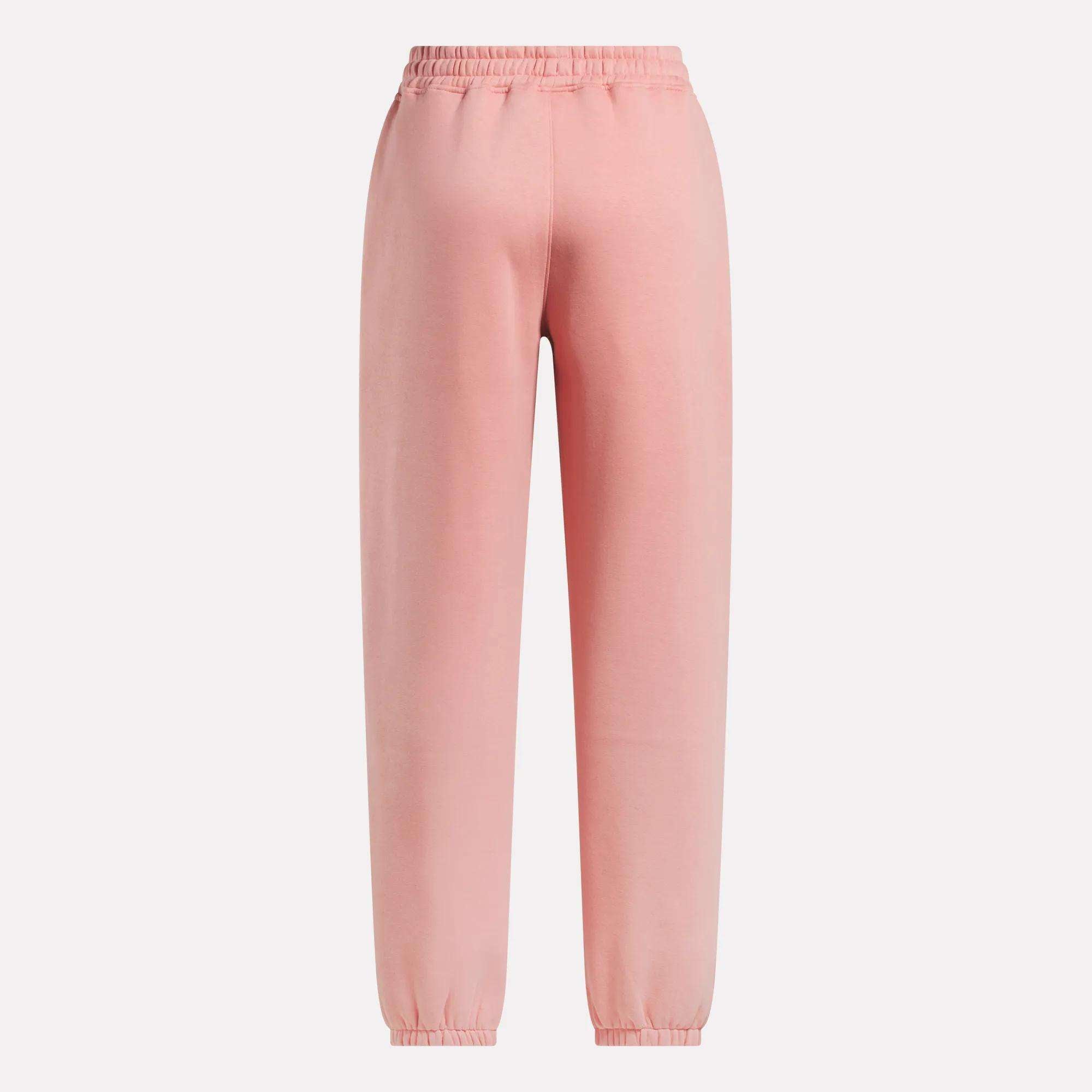 The Reebok Women's Wardrobe Essentials Sweat Pants in light pink feature an elastic waistband, ankle cuffs, and soft fleece material, shown against a plain white background.