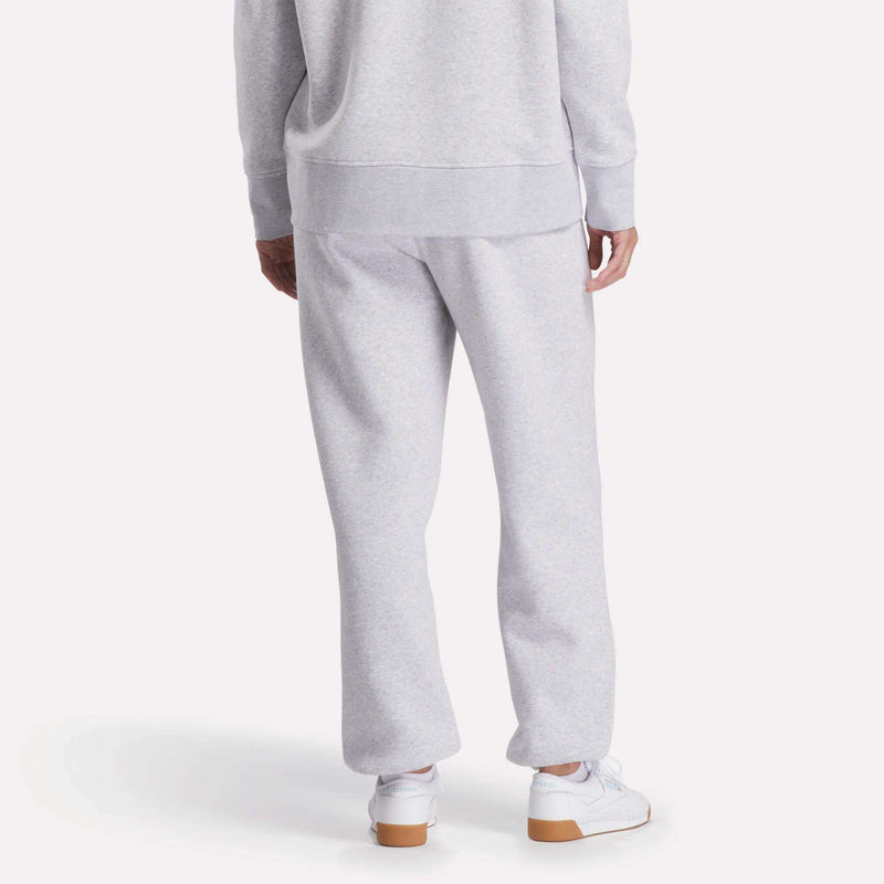 A person stands facing away in light gray Reebok Women's Wardrobe Essentials Sweat Pants and a matching sweatshirt, paired with white sneakers against a plain white background.