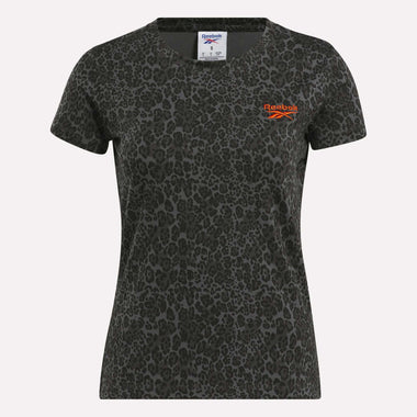 The Reebok Women's Leopard Print Baby T-Shirt features short sleeves, a bold black leopard print, and an orange logo on dark grey—ideal as a trendy mini tee.