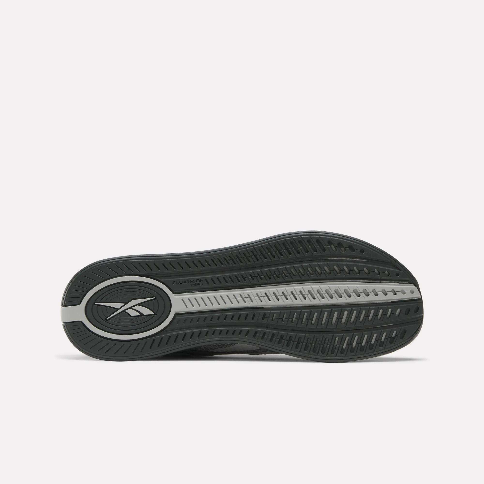 The image shows the sole of a dark-colored Reebok Nano X4 Training Shoe with a textured grip pattern, central groove, and oval Reebok logo near the heel—featuring Floatride Energy Foam cushioning.