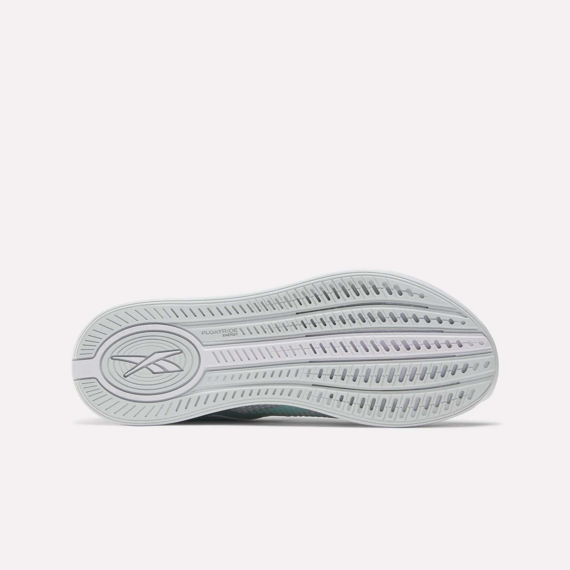 The image shows the sole of the Reebok Women's Nano X4 Training Shoes, featuring a wavy tread pattern with multiple grooves and a logo on the left side. The light gray sole is made with Floatride Energy Foam.