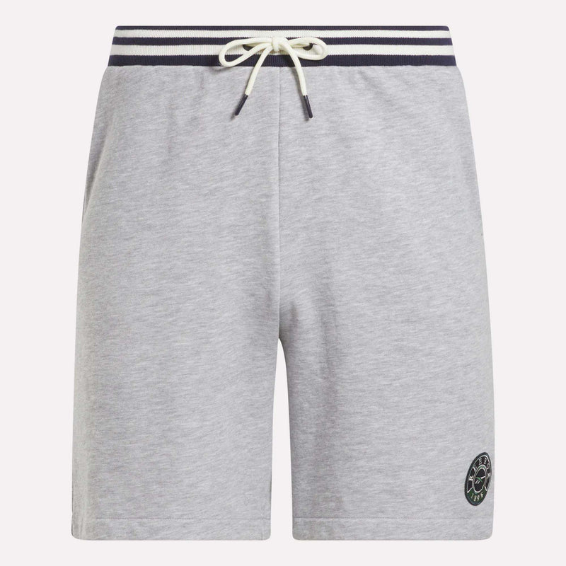 The Reebok Men's Lawn Club Shorts are light gray with a navy and white striped elastic waistband, white drawstring, side pockets, and a small circular logo on the lower left leg. Made from a comfortable cotton blend.
