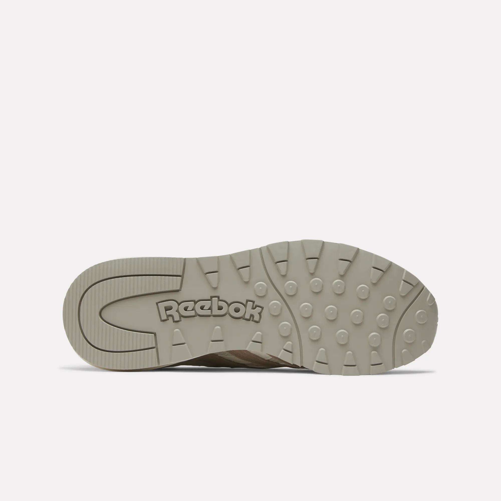 The image shows the beige rubber sole of the Reebok Women's Classic Nylon 89 Shoes, viewed from underneath. Circular grip patterns and an embossed Reebok logo near the heel highlight its retro design.