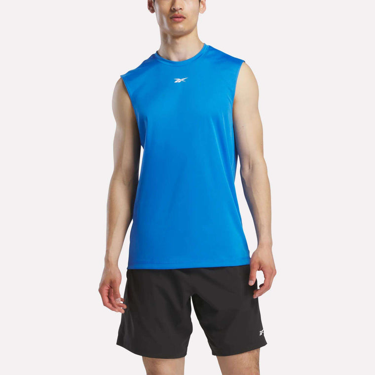 A man wears a Reebok Men's Sleeveless Tech Training T-Shirt in bright blue and black shorts, standing facing forward against a plain white background.
