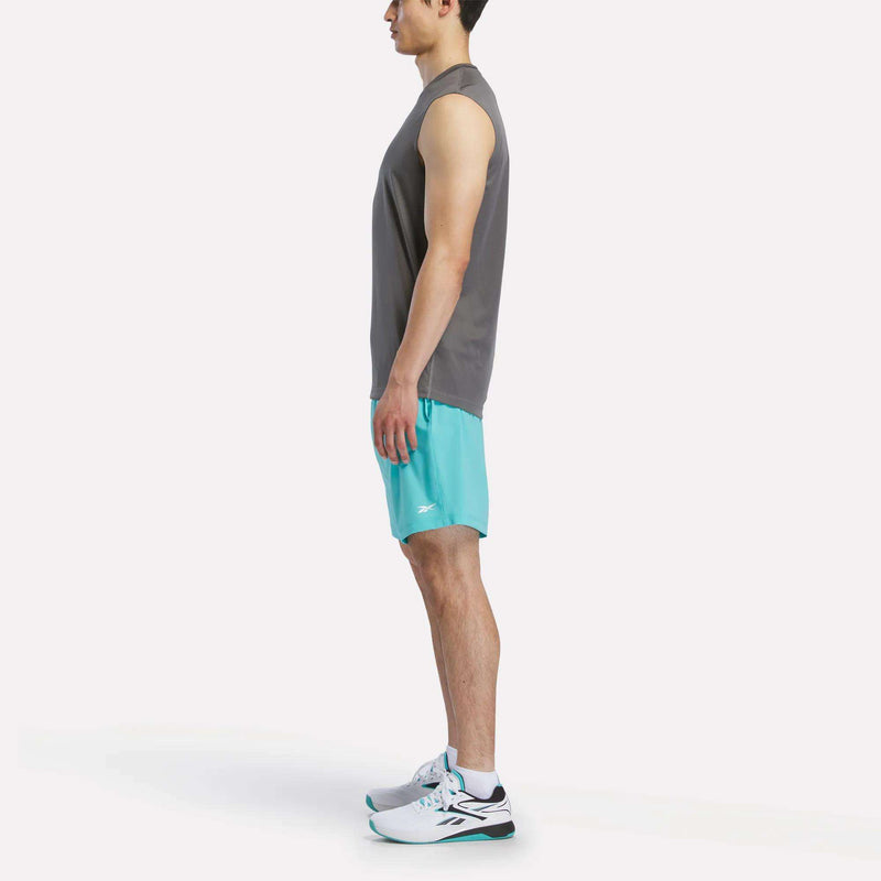 A man in profile wears a Reebok Men's Sleeveless Tech Training T-Shirt, turquoise athletic shorts, and white running shoes with teal and black accents against a plain white background.