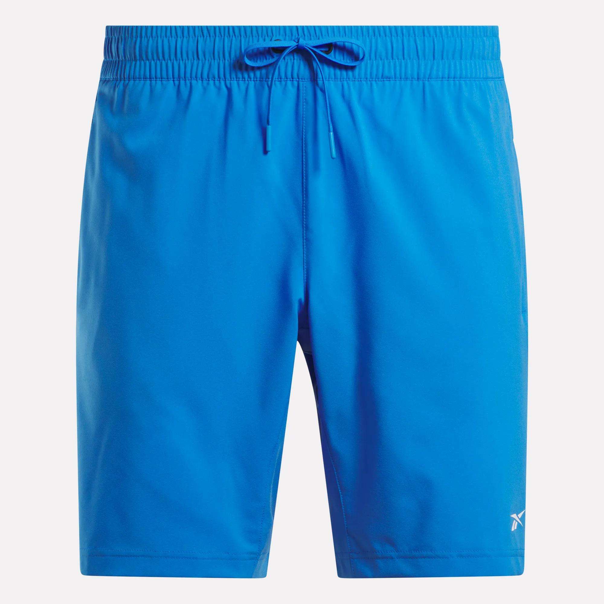 Men’s Woven Shorts by Reebok in bright blue with an elastic waistband, drawstring, and a white logo on the lower left leg. These sweat-wicking workout shorts are shown against a plain white background.