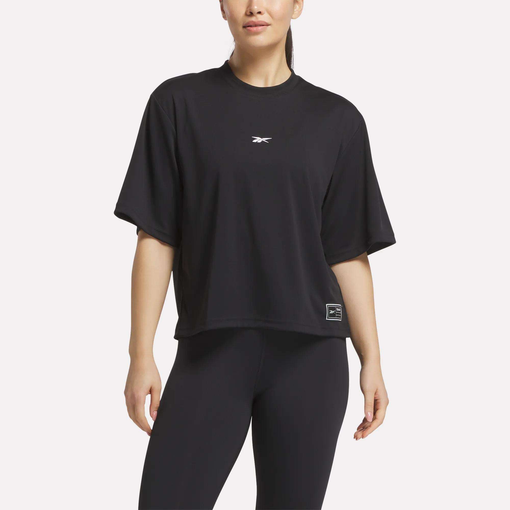 A woman wears a loose black Reebok Women's Basketball Mesh T-Shirt with a small chest logo and a label near the hem, paired with black leggings, standing against a plain white background.