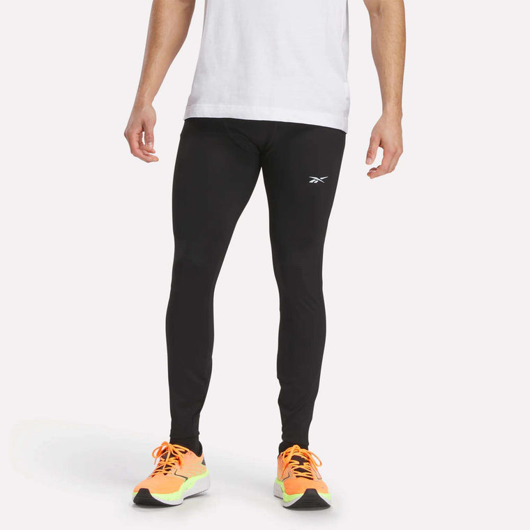 A person in a white t-shirt, bright orange running shoes with yellow soles, and black Reebok Men's Athlete Speed Running Tights stands against a plain light background.
