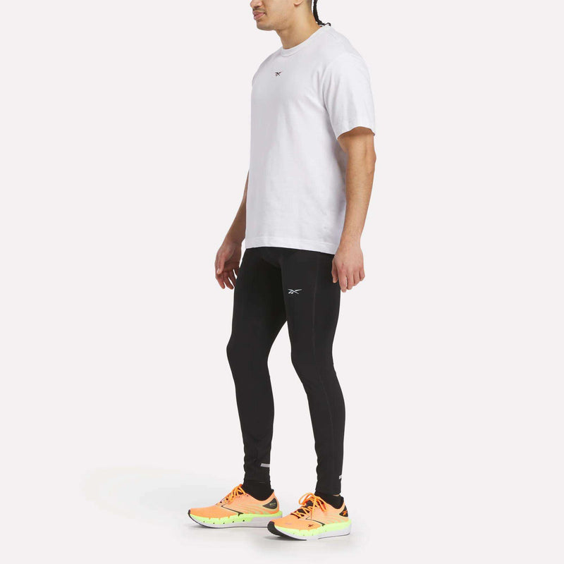 A person in a white t-shirt, Reebok Men's Athlete Speed Running Tights, and bright orange and yellow athletic shoes stands against a plain white background.