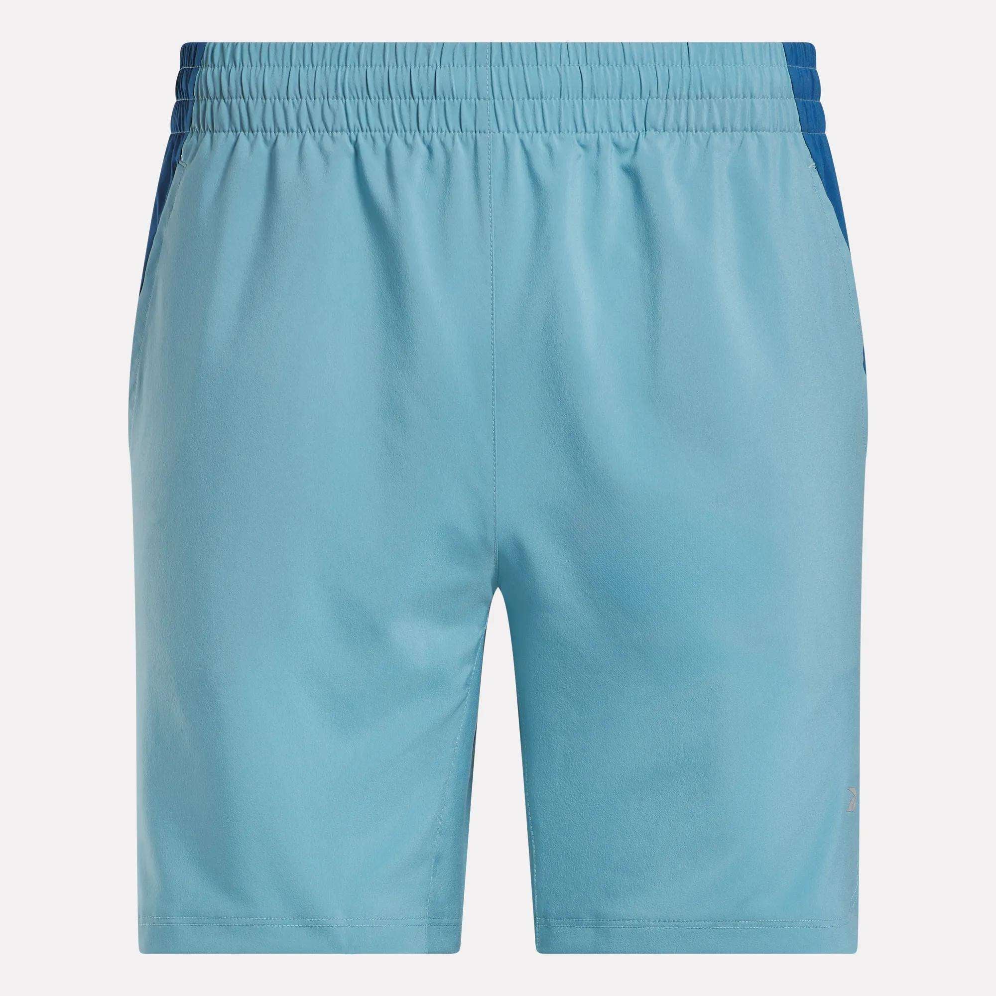 The Men’s Run Shorts by Reebok are light blue running shorts with an elastic waistband, subtle dark blue side accents, and comfortable inner tights, shown against a white background.