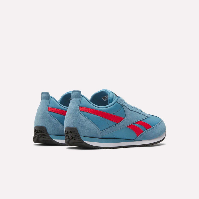 Reebok R100 Shoes: blue suede, low-profile sneakers with red side stripes and black soles, inspired by '70s running style, shown on a plain white background at an angle highlighting the back and outer sides.
