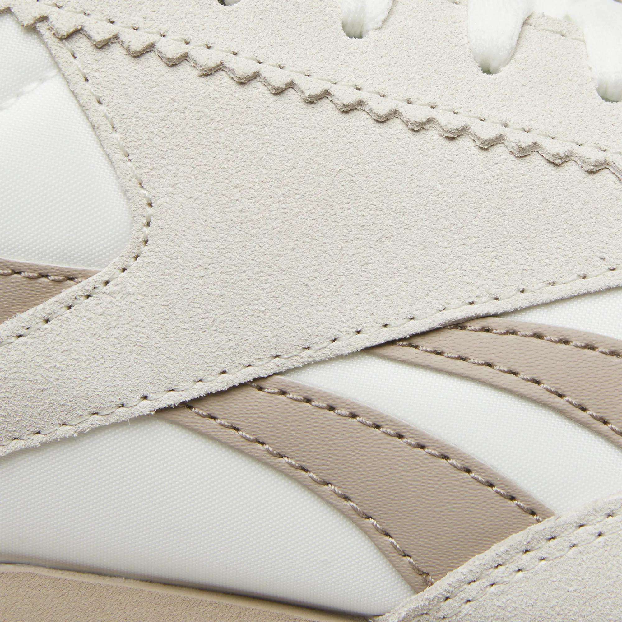 Close-up of Reebok R100 Shoes highlighting beige suede overlays, white textile uppers, and taupe synthetic stripes with detailed stitching. These low-profile sneakers feature layered textures and wavy edges inspired by '70s running styles.