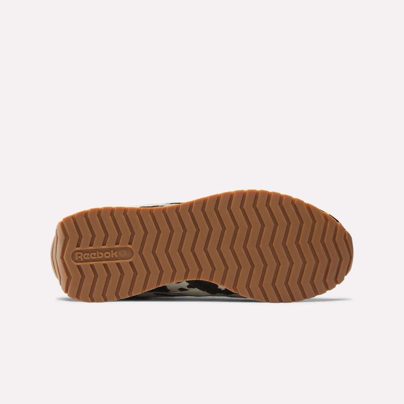 The image shows the bottom of the Reebok Women's Classic AZ Shoes with a tan, zigzag-patterned rubber sole and the embossed Reebok logo near the heel, highlighting their stylish design.