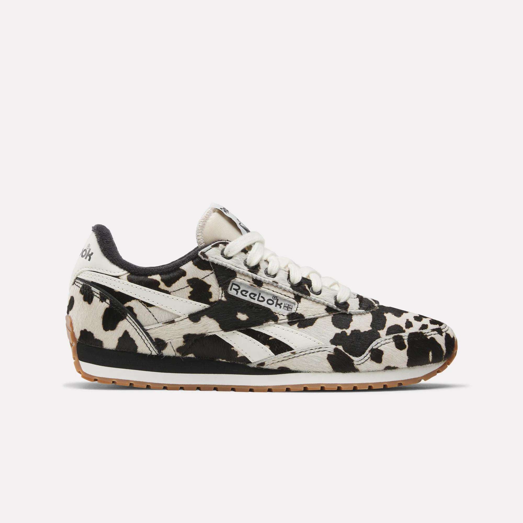 The Reebok Women's Classic AZ Shoes feature a bold animal print cow pattern, white laces, black sole trim, a light brown rubber outsole, and visible Reebok logos—perfect for any women’s sneaker collection.