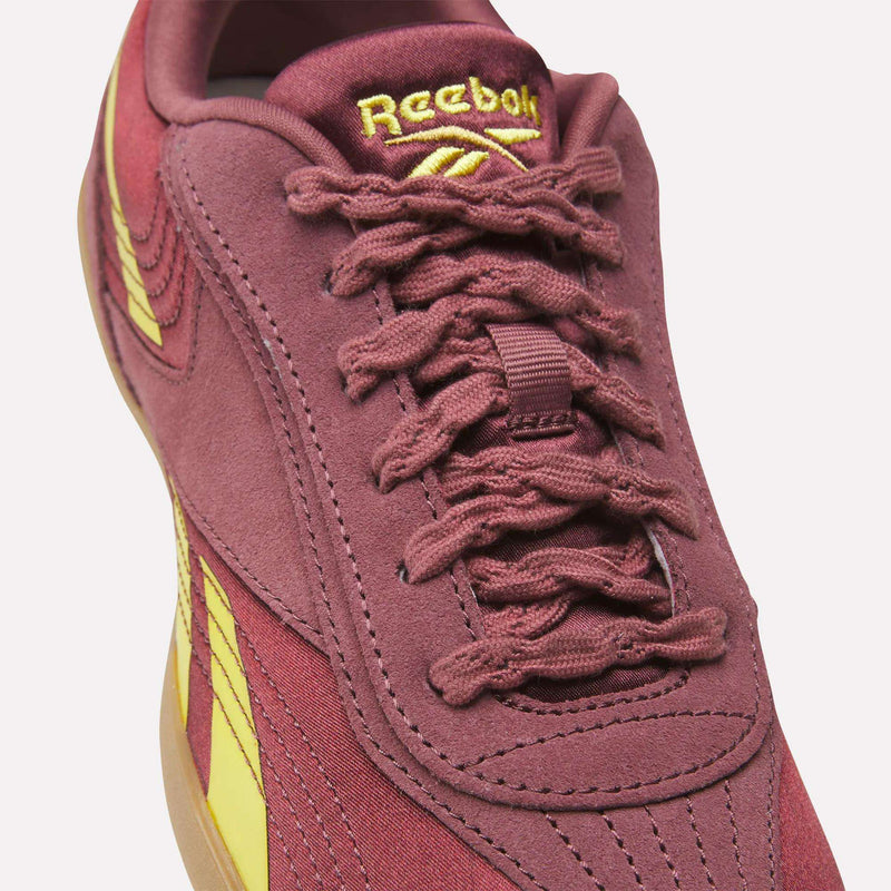 Close-up of the Reebok Women's Ultra Lo Shoes in maroon, with yellow branding and accents. This lightweight, low-profile shoe features a woven lace design, gum-colored sole, and detailed stitching.