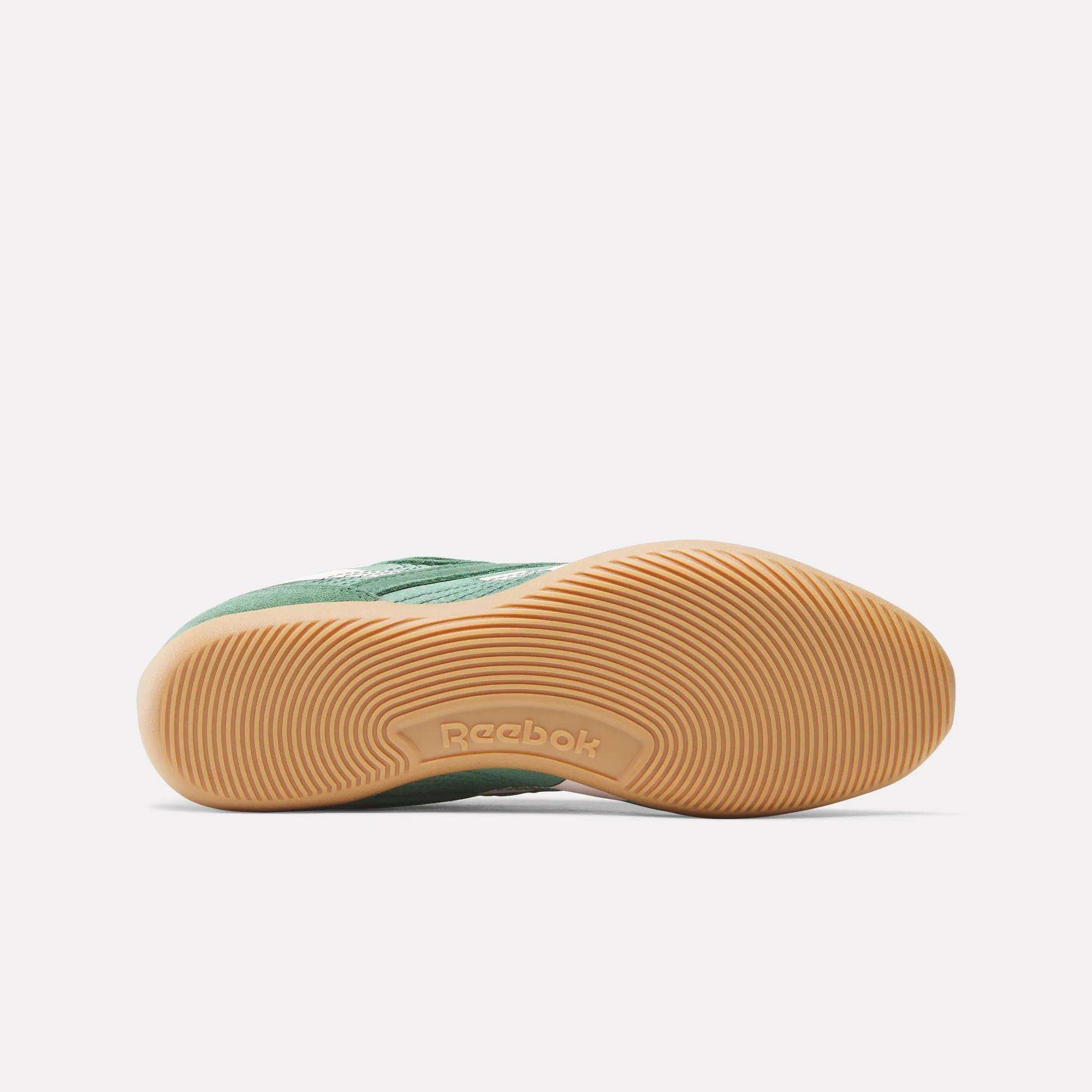 The image displays the sole of a green Women's Ultra Lo Shoe by Reebok, featuring a tan rubber bottom with a circular tread and an embossed Reebok logo in the center. The shoe rests on its side against a plain white background.