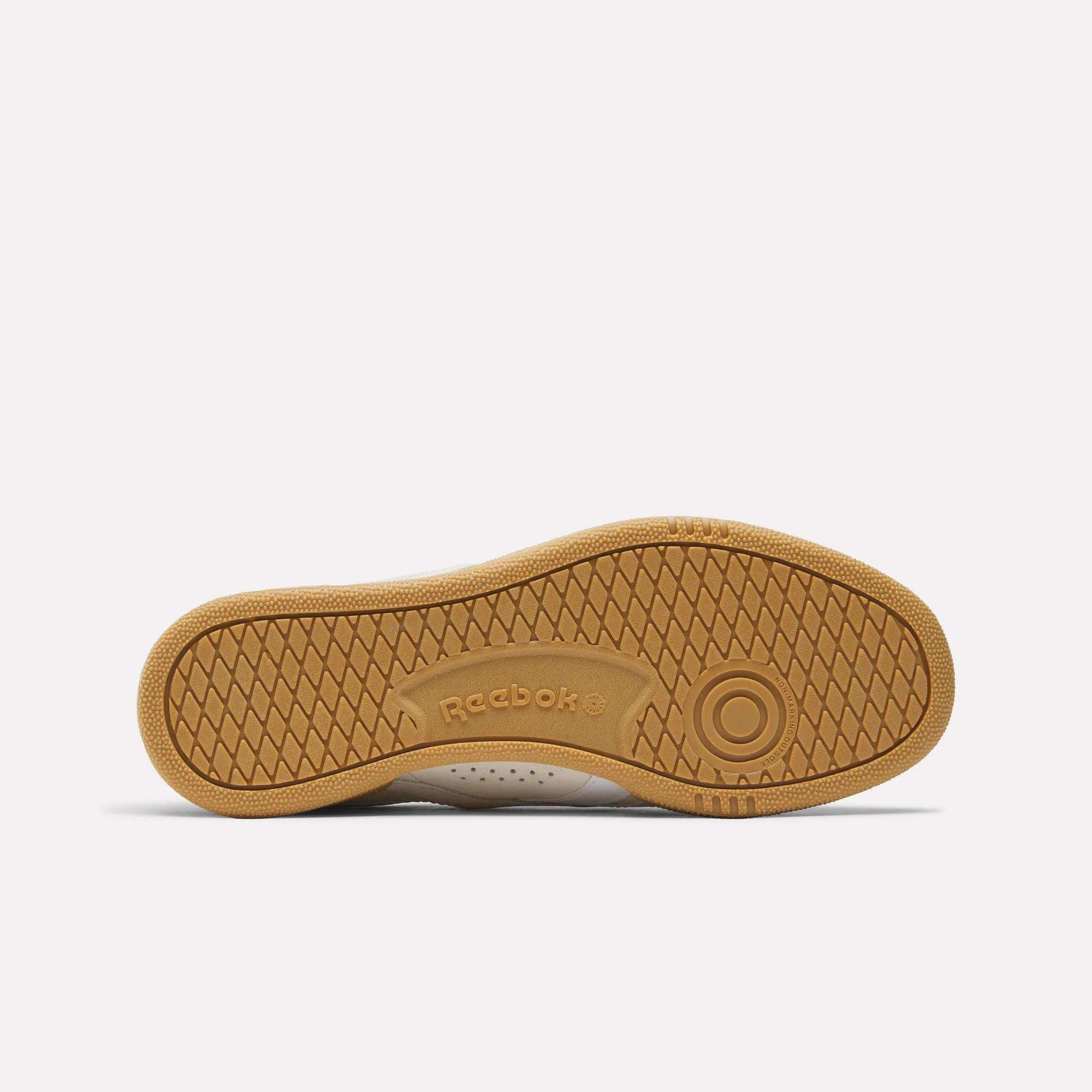 Bottom view of the Reebok Club C Grounds UK Shoes shows a tan rubber sole with a textured herringbone pattern and the Reebok logo embossed near the center, emphasizing its classic style.
