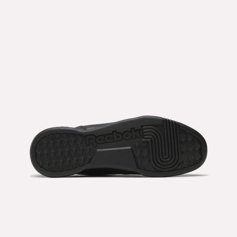 The image displays the black rubber outsole of Reebok Women's Workout Plus Shoes, showing the Reebok logo and textured tread for grip. The sole-up view on a white background highlights the classic '80s fitness-inspired design.