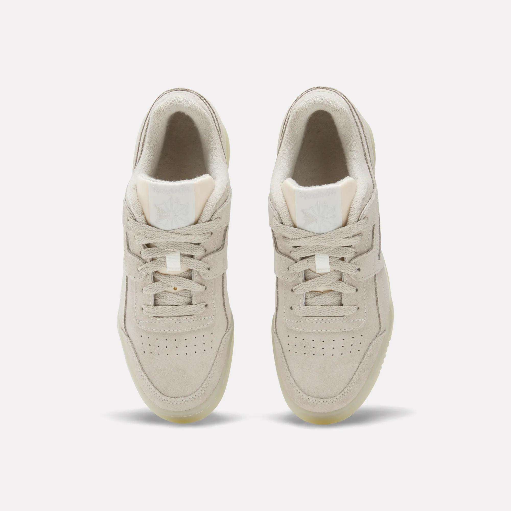 A pair of beige suede Reebok Women's Workout Plus Shoes with white soles are viewed from above, displaying laces, perforated toe boxes, and branded tongues. These classic sneakers evoke '80s fitness style against a plain white background.
