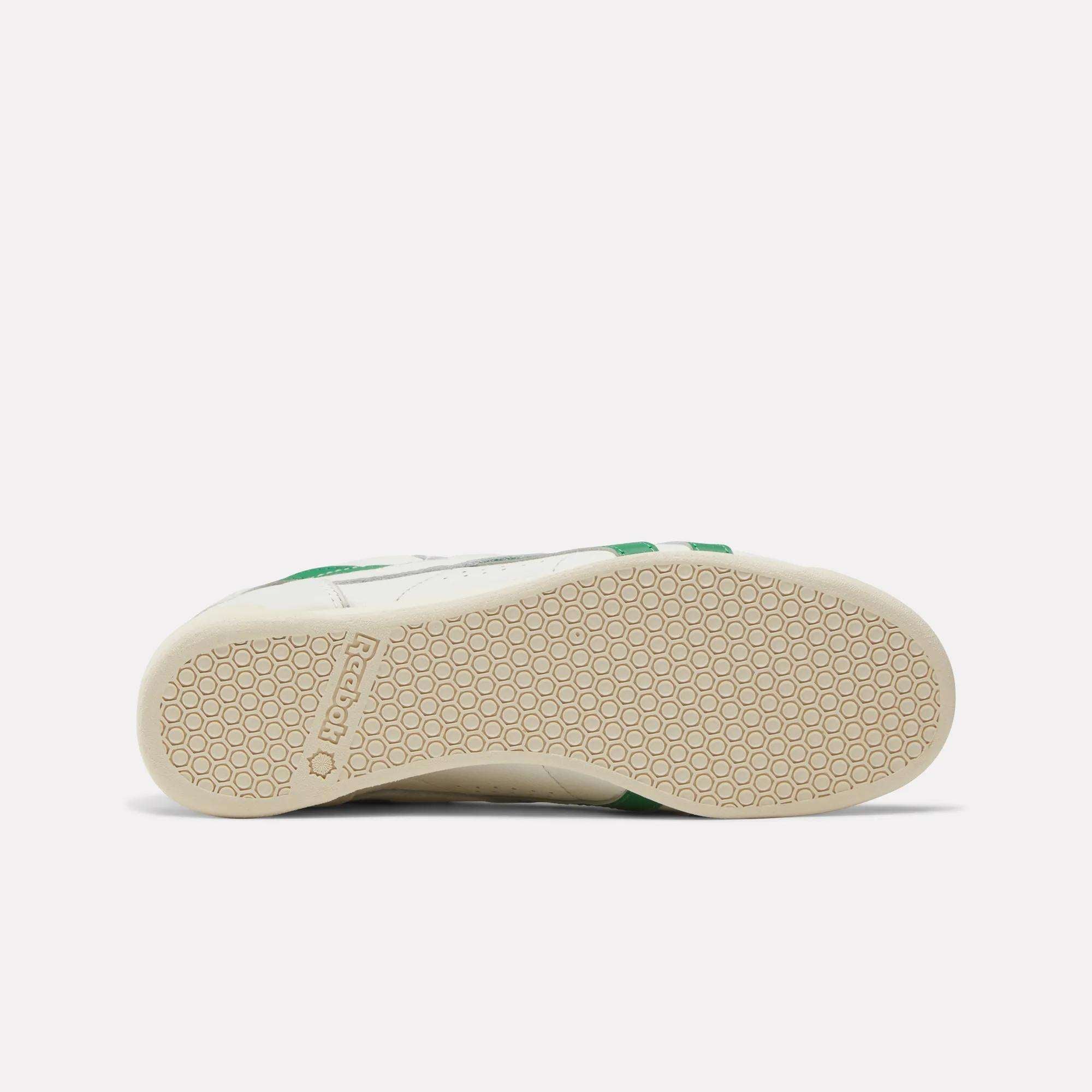 The Reebok Women's Freestyle Lo Shoes are white with a beige sole, feature a hexagonal tread pattern, an EVA midsole, and display the Reebok logo near the heel.