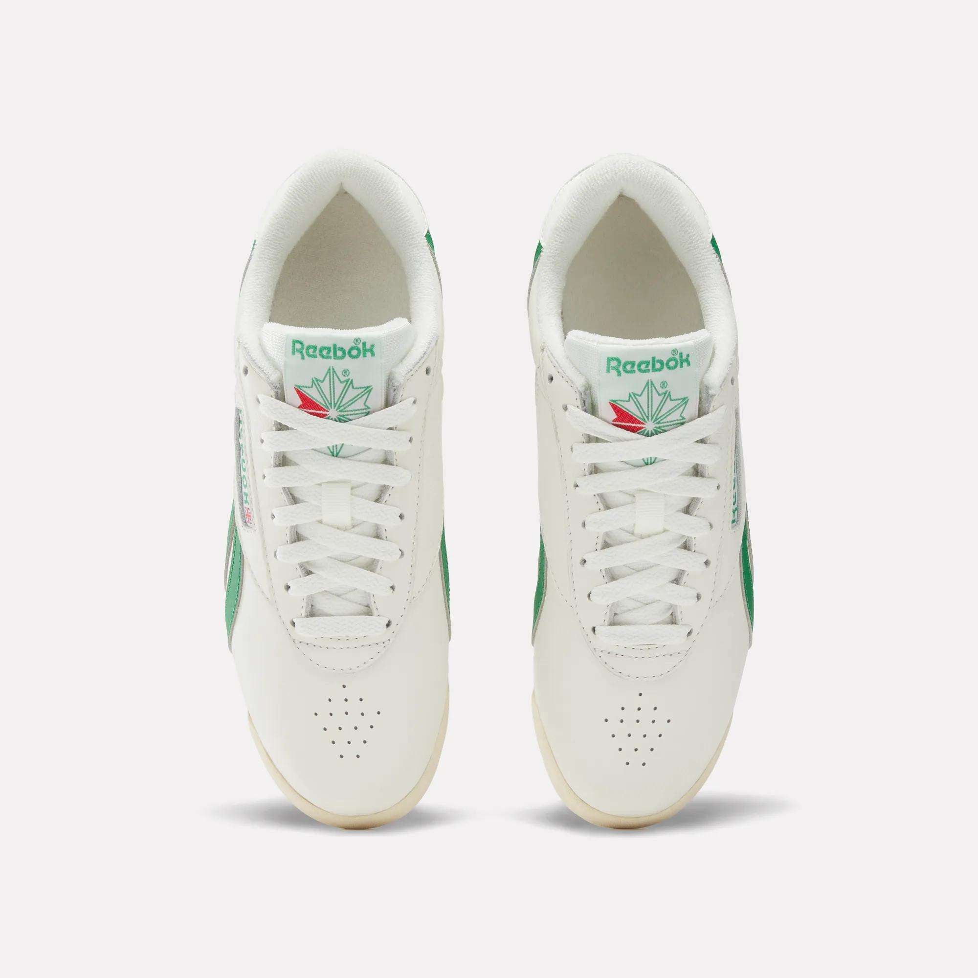 Top view of Reebok Women's Freestyle Lo Shoes in white leather with green accents, white laces, and a tongue logo featuring green and red. Set on a light background. EVA midsole offers extra comfort.
