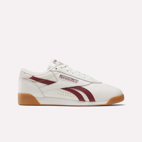 The Women’s Freestyle Lo Shoes by Reebok feature a white upper with maroon accents, maroon side stripes, gum sole, and Reebok logos on the side and tongue—shown on a plain light background.