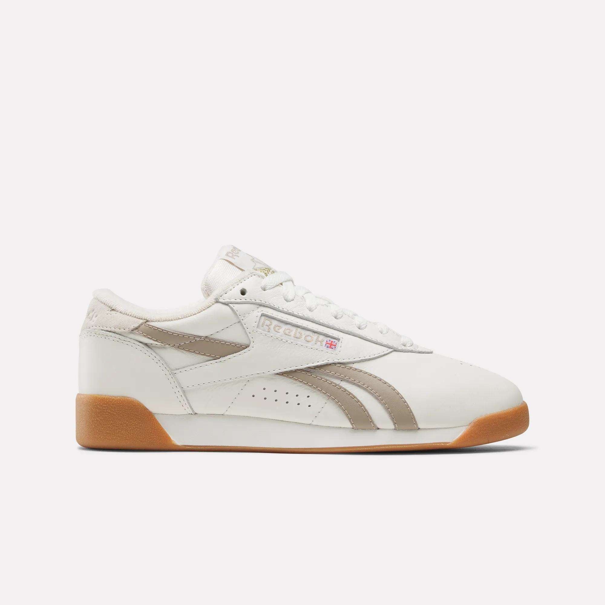 The Reebok Women's Freestyle Lo Shoes are retro white sneakers with beige accents, a gum sole, and the Reebok logo on the side. Their classic, low-cut design and white laces offer timeless style.