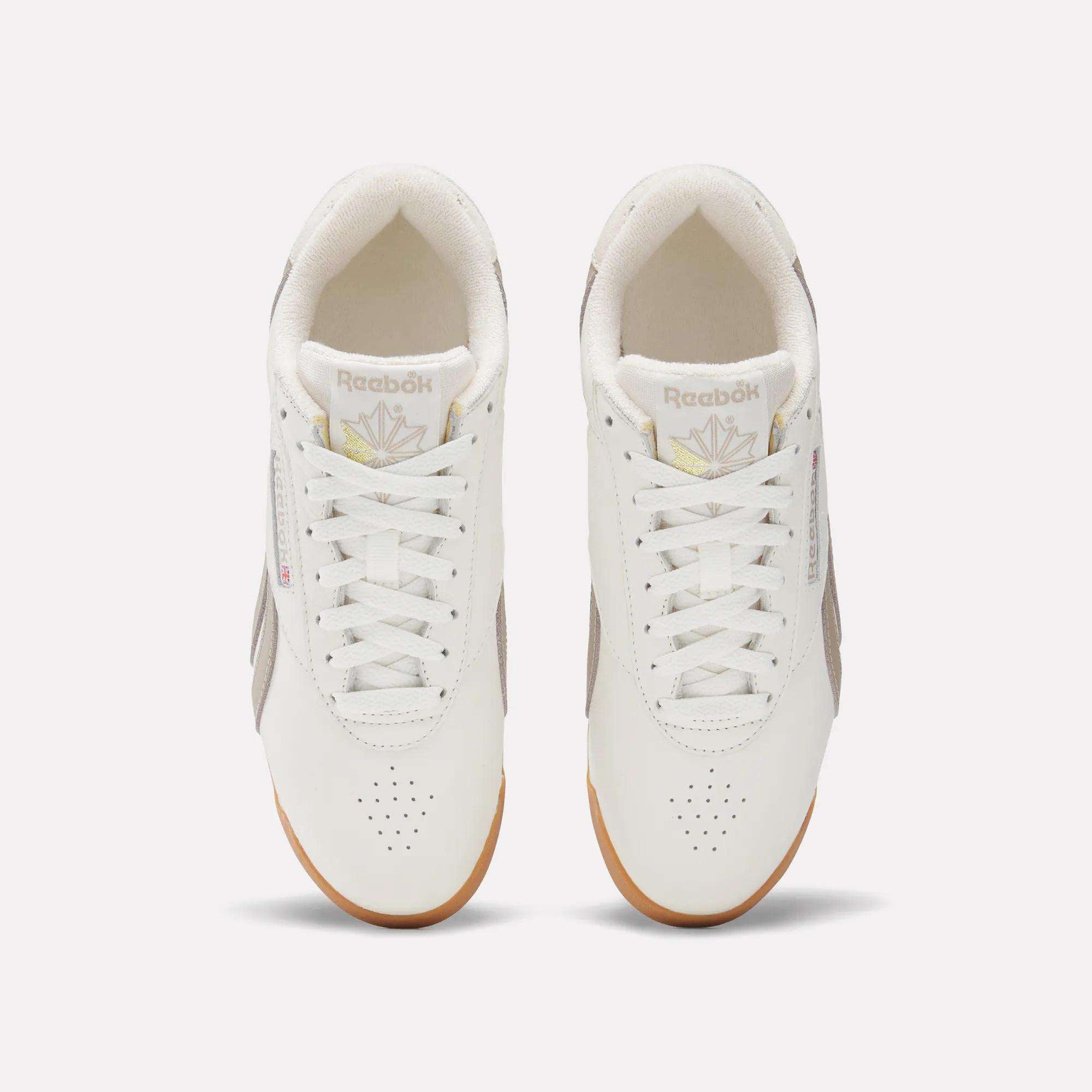 A pair of Women's Freestyle Lo Shoes by Reebok with white uppers, beige side panels, and gum soles is viewed from above on a plain light background. The Reebok logo appears on the tongues and sides of these classic sneakers.