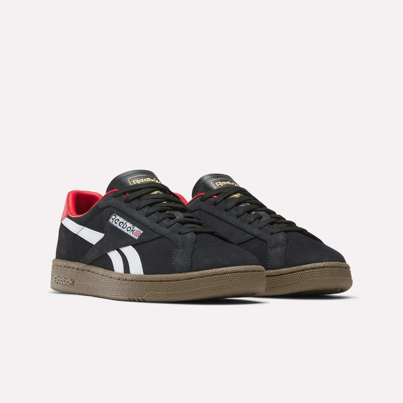 The Reebok Club C Grounds UK Shoes feature a black design with white side stripes, brown rubber soles, and red inner collar accents, blending classic tennis style into casual footwear. Displayed on a plain white background.