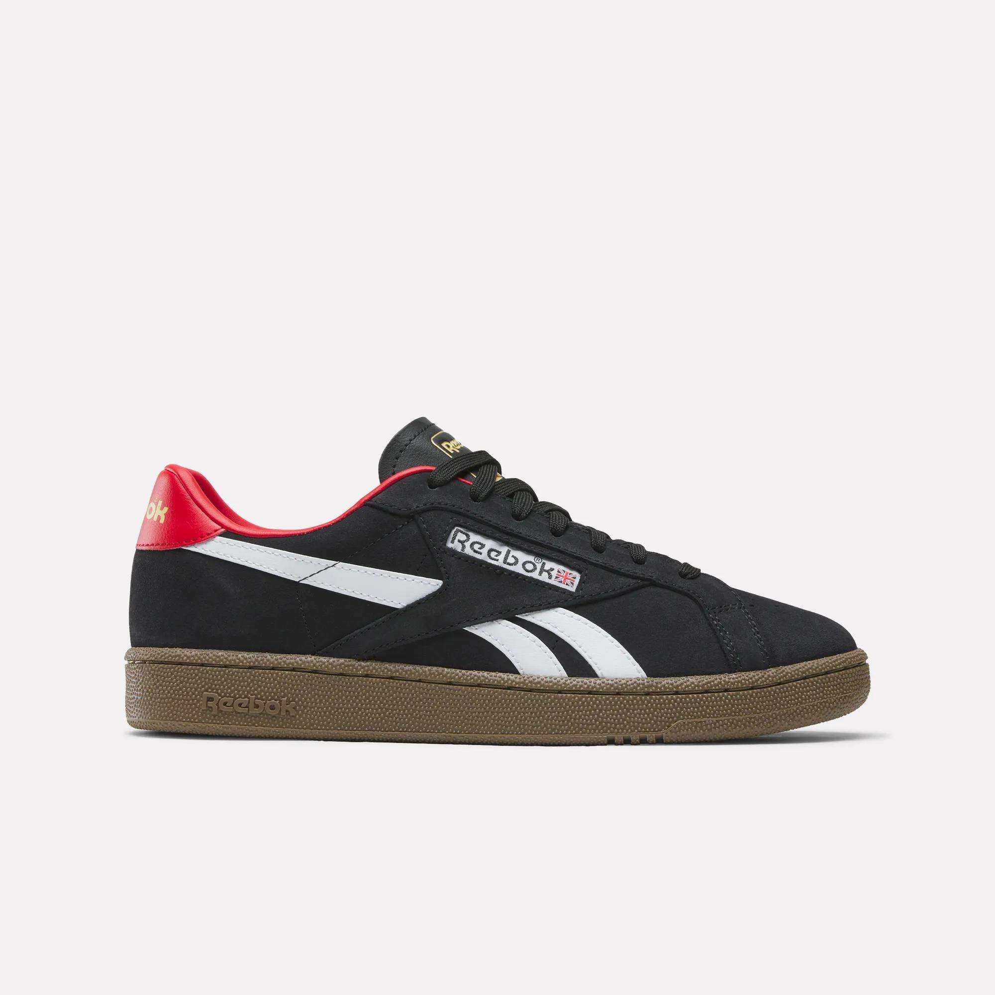 The Reebok Club C Grounds UK Shoes in black feature white side stripes, a brown sole, red heel detail, and gold tongue logo, shown in side profile on a plain white background—ideal casual sneakers with classic tennis flair.